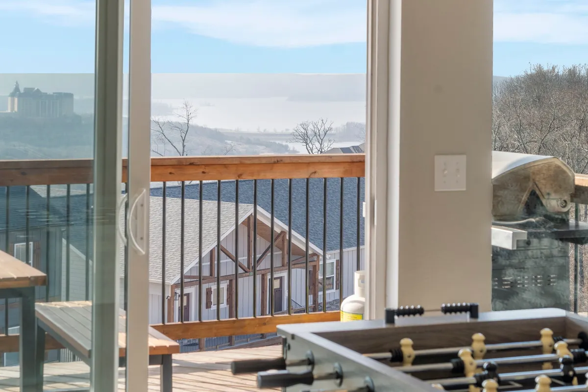 A balcony setup with a foosball table, outdoor grill, and seating area overlooking a scenic backdrop. The space is designed for playful competition, barbecuing, and enjoying time with friends as the sun sets.