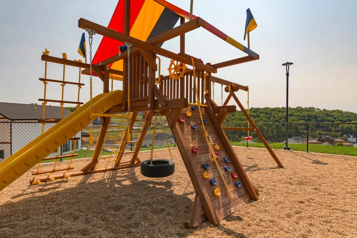 A lively playground structure with slides, a rock climbing wall, and tire swing where children are joyfully playing. Colorful flags and a festive atmosphere capture the spirit of community and family-friendly fun.