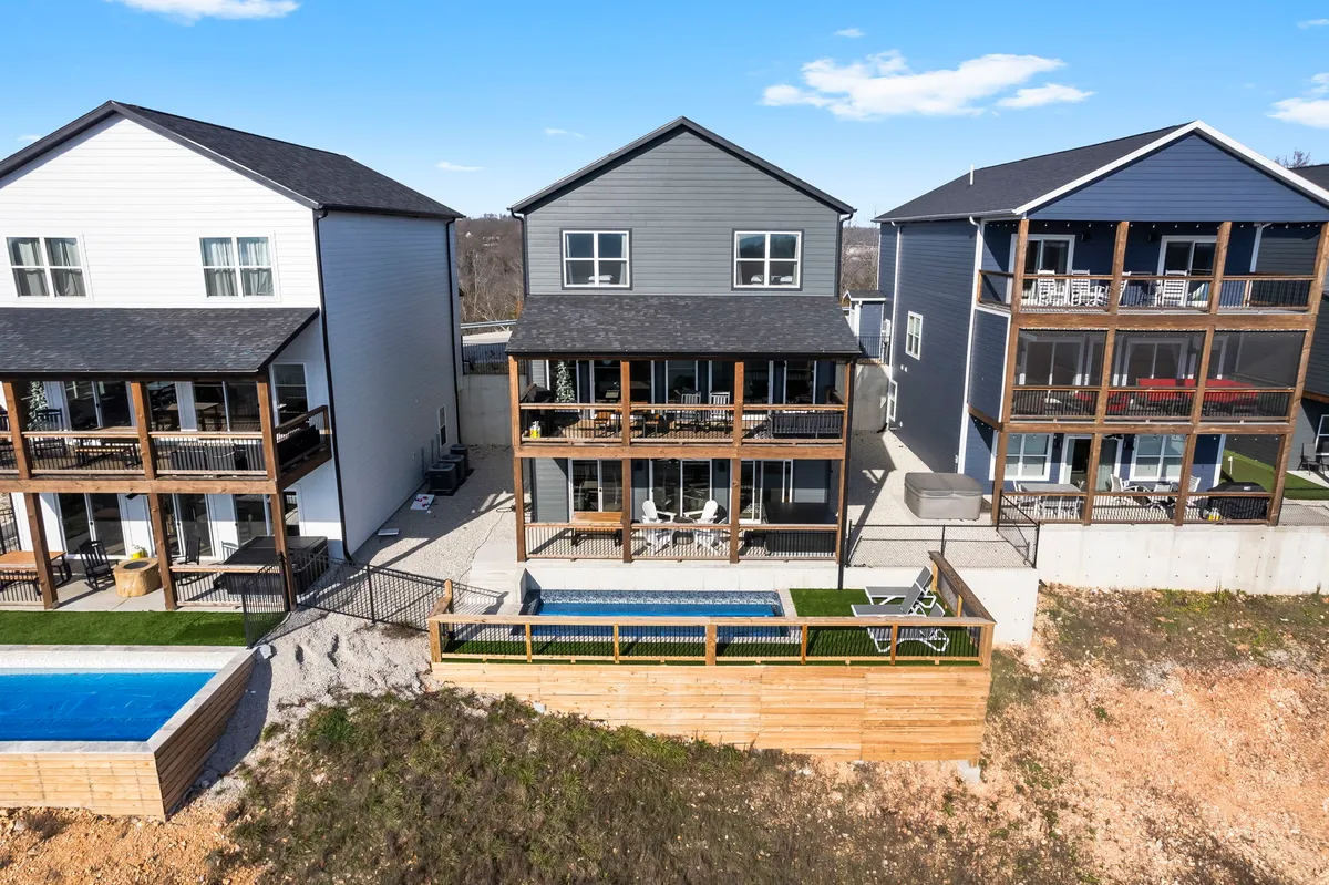 This exterior image features three modern houses, each with their own deck and outdoor seating areas, all overlooking a swimming pool and a landscaped yard. The scene captures a lively and inviting environment perfect for gatherings and group activities.