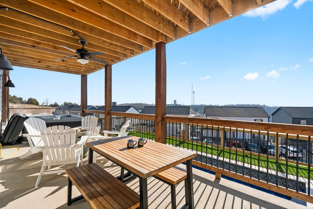 A spacious wooden deck featuring a hot tub, an outdoor dining table with chairs, and sweeping views of the surrounding area. The scene evokes a lively, social atmosphere perfect for group gatherings, relaxing soaks, and sunset celebrations.