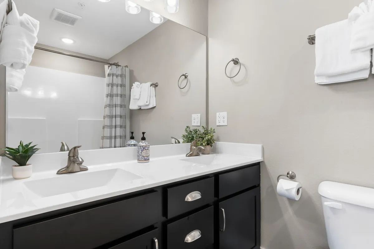 A modern bathroom with double sinks, a decorative plant, and fresh towels artfully arranged. The space feels fresh, inviting, and designed for easy morning and evening routines.