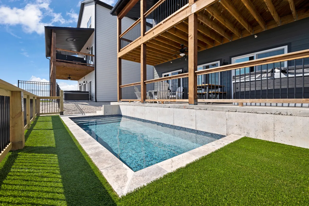 An inviting exterior scene featuring a sparkling swimming pool surrounded by a wooden deck, multiple balconies, and comfortable lounging areas. The setting is enhanced by the warm glow of sunset, hinting at opportunities for relaxing swims or gathering outdoors with scenic lake views. The landscape and architecture evoke a sense of luxury and leisure.