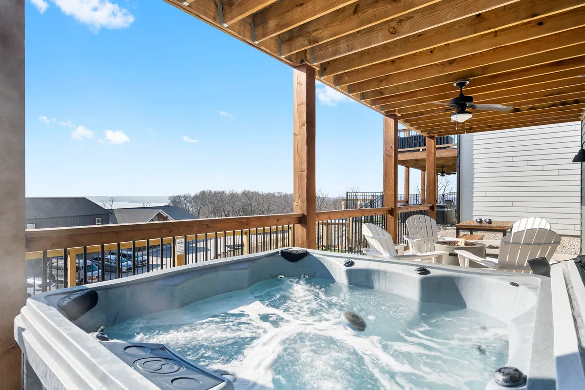 This exterior view spotlights a hot tub beneath a wooden ceiling, surrounded by Adirondack chairs and a scenic landscape. The warm, inviting ambiance makes it ideal for soaking sore muscles or stargazing in the evening.