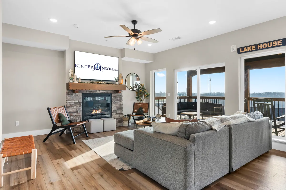 A spacious open-concept living area, featuring a cozy fireplace as the focal point. Comfortable seating is arranged around the fireplace and TV, with large windows allowing natural light to flood the room. The inviting atmosphere is perfect for gatherings, relaxation, and entertainment.