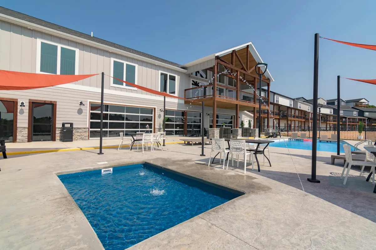 This exterior image features a private swimming pool with an adjacent hot tub, surrounded by an inviting outdoor seating area and set against the backdrop of the building's facade. String lights overhead set a festive, resort-like mood, while the pool and hot tub are clear focal points.
