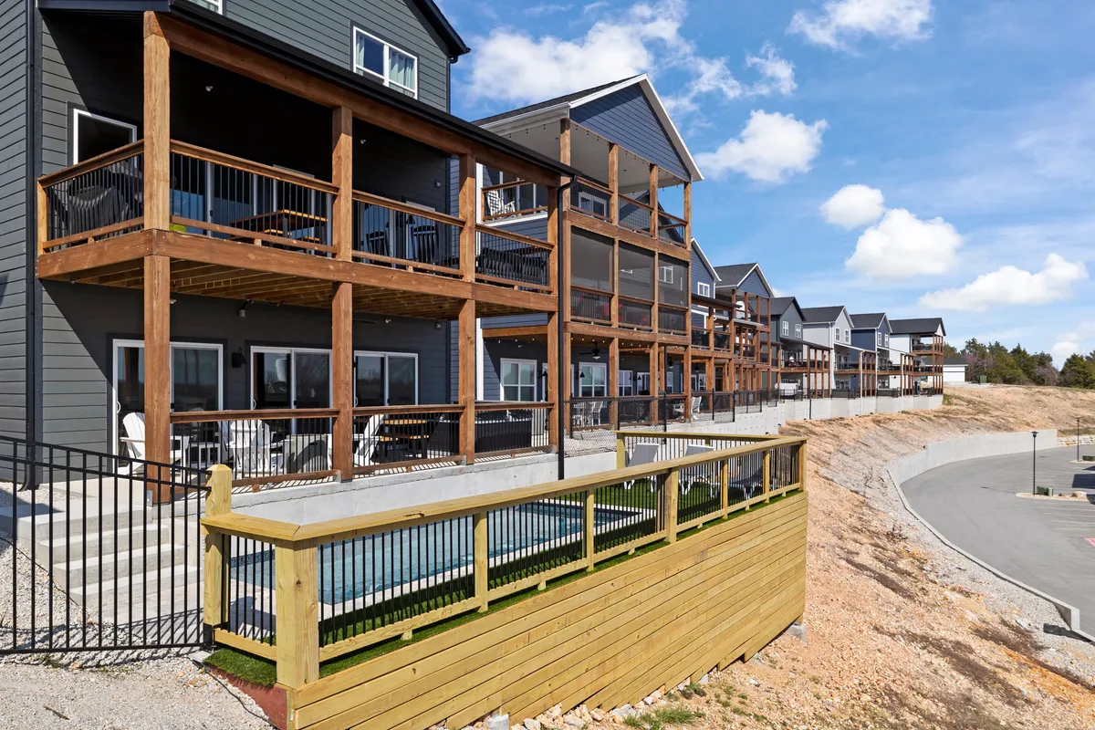 This exterior image showcases modern architectural balconies and a wooden railing overlooking landscaped grounds. The multiple balconies offer spaces for outdoor socializing, enjoying the view, or unwinding after group activities. The setting is inviting and visually connects the Lodge with its scenic surroundings.